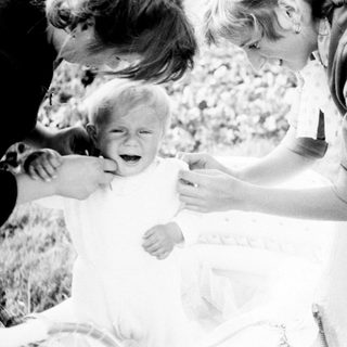 Here's a brief summary of the image: A person assists a young child into a white garment.