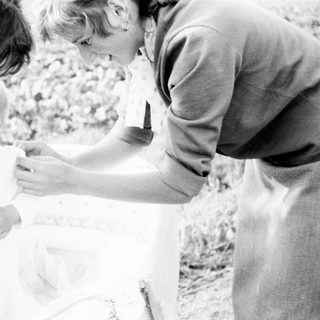 Here's a brief summary of the image: A person assists a young child into a white garment.