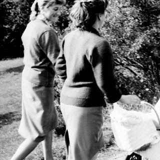 Two women walk along a path with a baby carriage.