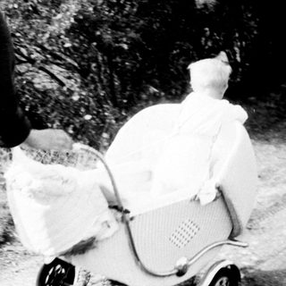 Two women walk along a path with a baby carriage.
