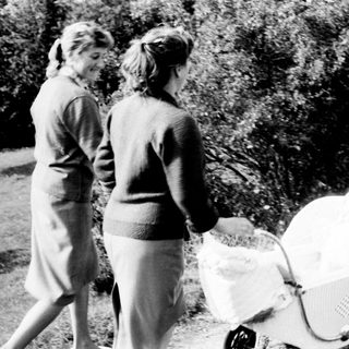 Two women walk along a path with a baby carriage.