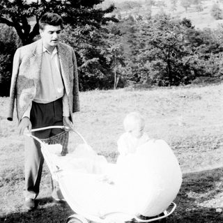 Man pushing a baby in a vintage stroller outdoors.