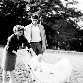 Couple stands near a baby in a vintage wicker pram.