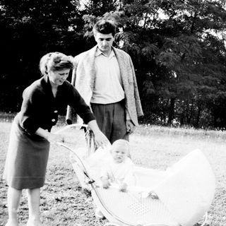 Couple stands near a baby in a vintage wicker pram.