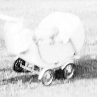 Woman pushing a vintage baby carriage across a lawn.