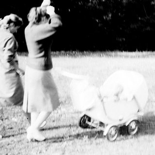 Woman pushing a vintage baby carriage across a lawn.