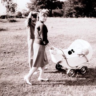 Woman walks with a vintage baby carriage in a field.