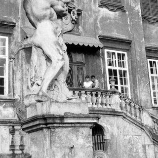 Statue and people on a balcony of an old building.