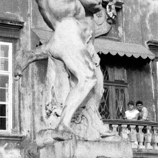 Statue and people on a balcony of an old building.