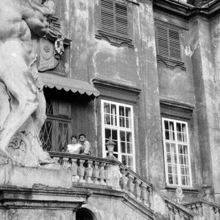 Here's a brief summary of the image: People on a balcony overlooking a grand, aged building.