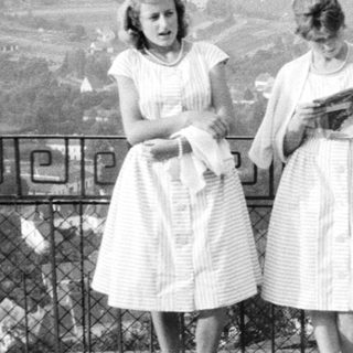 Three women in vintage dresses stand near a fence.