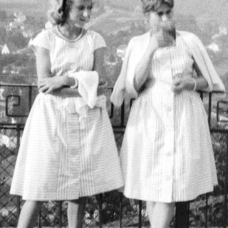 Three women in vintage dresses stand near a railing.
