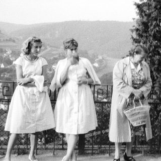 Three women in vintage dresses stand near a railing.