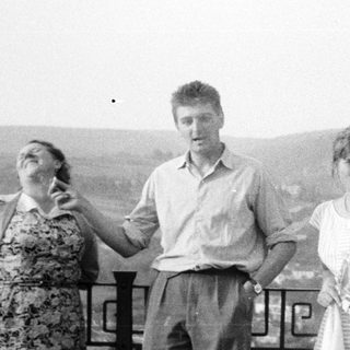 Three people stand outdoors, overlooking a landscape with a tree.