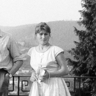 Three people stand outdoors, overlooking a landscape with a tree.