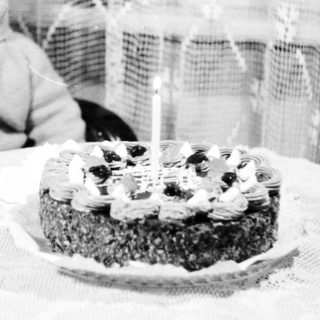 Child sits near a cake with a single candle.