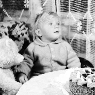 Child sits near a cake with a single candle.