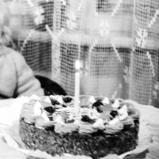 Child with teddy bear sits near birthday cake.
