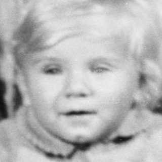 Child with teddy bear sits near birthday cake.