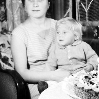 Woman holding child, seated near a cake.