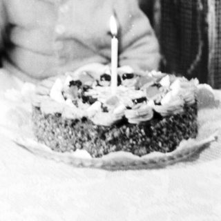 Child sits with a woman, looking at a small cake.