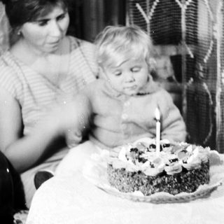 Child sits with a woman, looking at a small cake.