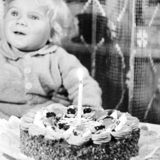 Baby sits near a cake with a single candle.