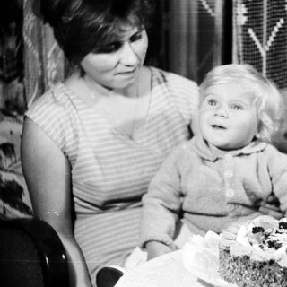 Baby sits near a cake with a single candle.