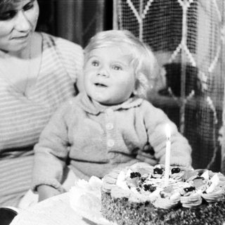 Baby sits near a cake with a single candle.