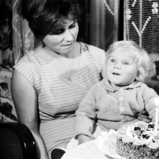 Baby sits near a cake with a single candle.