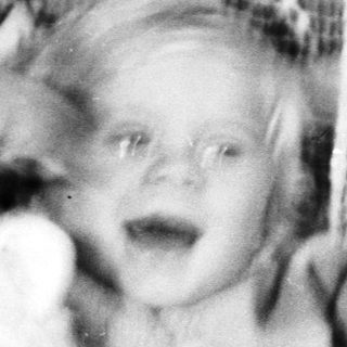 Black and white photo of a baby with a teddy bear.