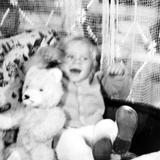 Black and white photo of a baby with a teddy bear.