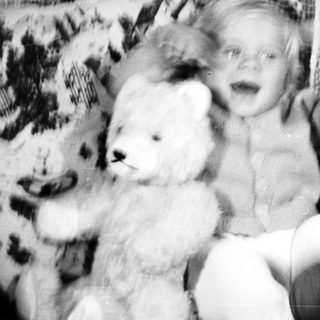 Black and white photo of a baby with a teddy bear.