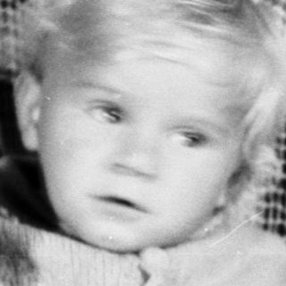 Baby sits with teddy bear in vintage chair.