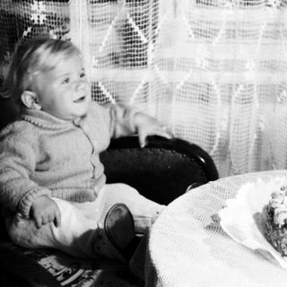Here's a brief summary of the image: Child sits near a cake with a single candle.