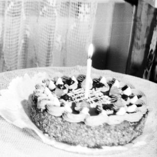 Here's a brief summary of the image: Child sits near a cake with a single candle.