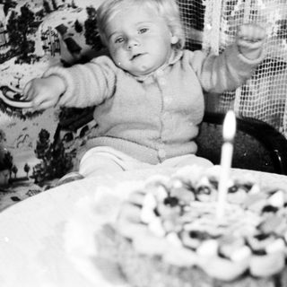 Baby sits in high chair, reaching for a cake.