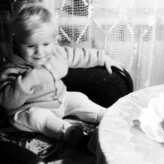 Baby sits in chair next to a birthday cake.