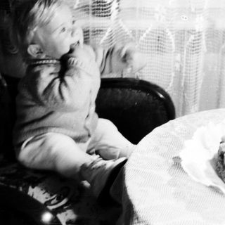 Child sits near a cake with a single candle.