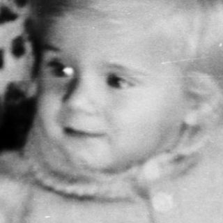 Baby sits near a cake with a single candle.