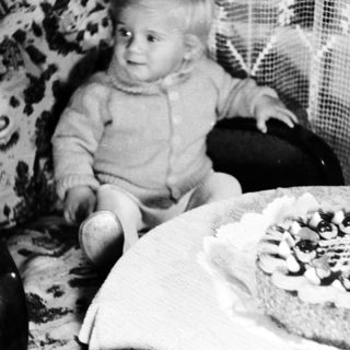 Baby sits near a cake with a single candle.