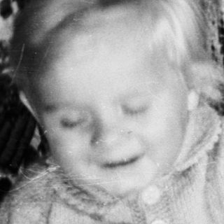 Here's a brief summary of the image: Baby sits near a small cake with a candle.
