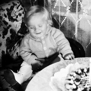 Here's a brief summary of the image: Baby sits near a small cake with a candle.