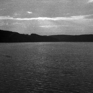 Dark, monochrome landscape with water and distant hills.