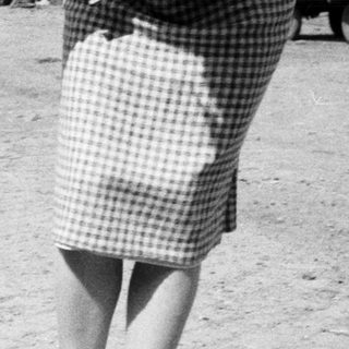 Baby in overalls walks with an adult outdoors.