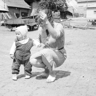 Baby takes first steps near a farmhouse, woman watching.
