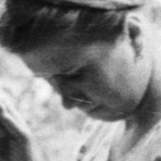 Woman sits outdoors, sewing in a garden setting.