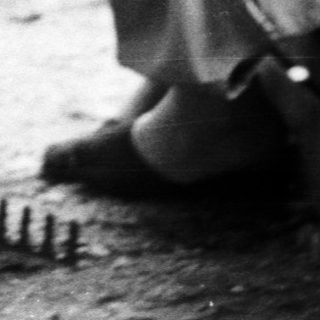Child stands near watering can, woman sits on crate.
