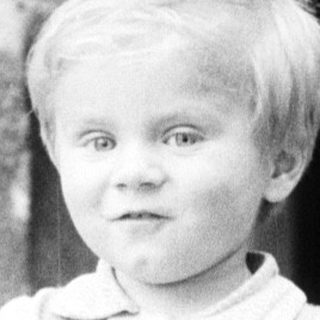 Young boy stands holding a toy, outdoors, vintage photo.