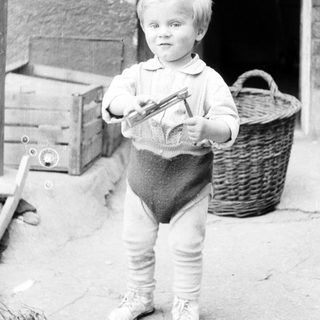 Young boy stands holding a toy, outdoors, vintage photo.